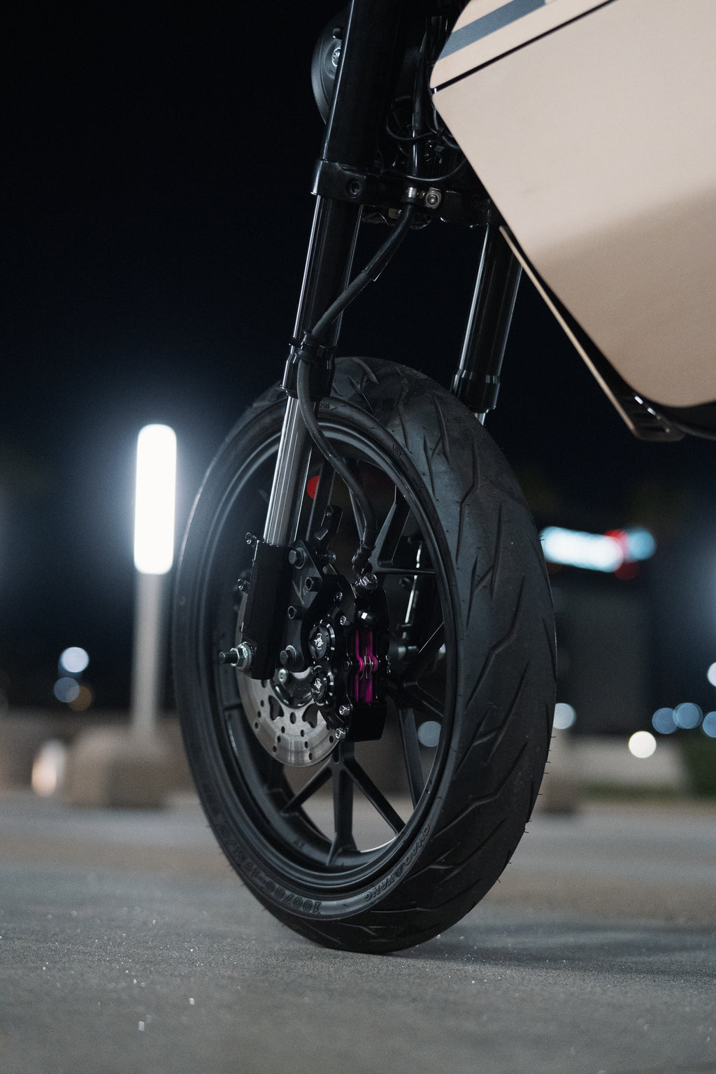 Close-up of a motorcycle wheel on a dark street with blurred lights in the background